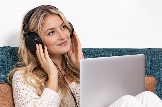 Ein junges Mädchen sitzt in einem Stuhl, hat einen Kopfhörer auf und hört Neuromusik. Sie macht ein genußvolles Gesicht.